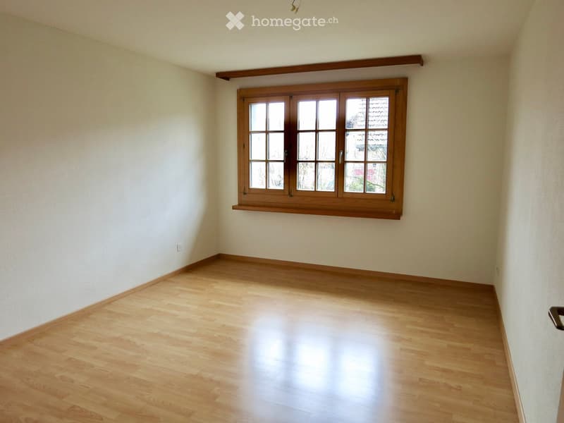 Empty room with light wooden flooring and white walls, featuring a large wooden-framed window with multiple panes.