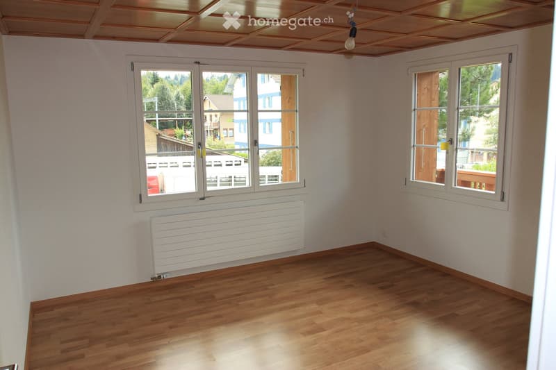 Empty room with wooden flooring, white walls, large windows, and a radiator. No furniture or equipment present.