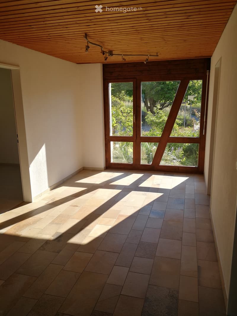 Empty hallway with tiled floor, wooden ceiling, and large windows leading to a garden area.