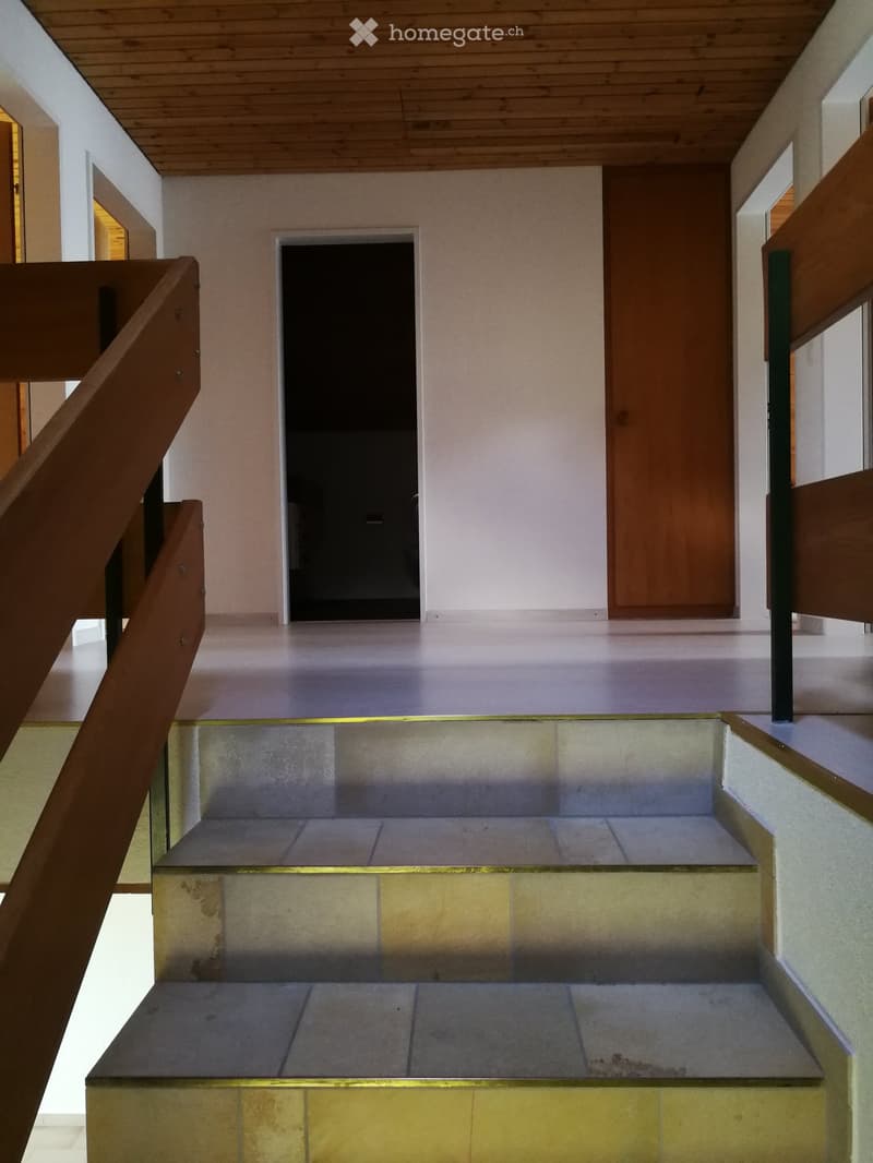 Staircase with wooden handrails and tiled steps leading to an open doorway, with light-colored walls and a wooden ceiling.
