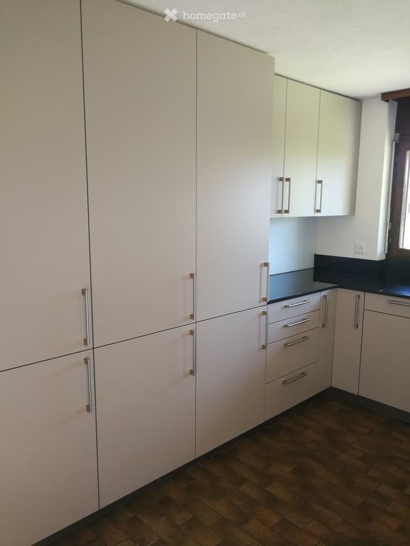 Modern kitchen with light-colored cabinets, silver handles, and wooden flooring.