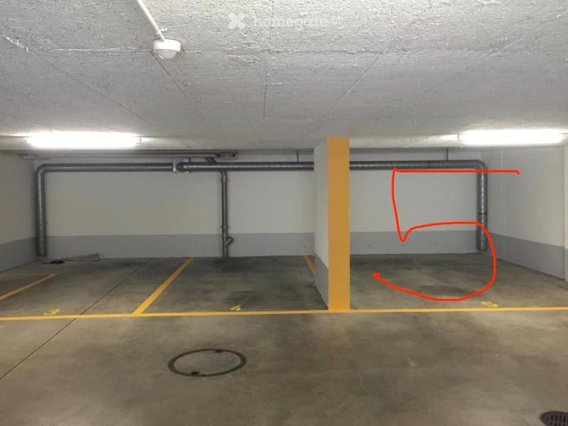 Underground parking space with concrete floors, grey walls, yellow parking lines, and a single marked parking spot outlined in red.
