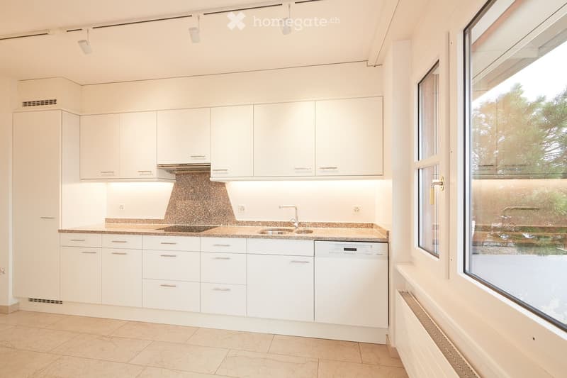 Modern kitchen with white cabinets, granite countertops, a sink, and a dishwasher. Large windows provide natural light and a view of greenery outside.