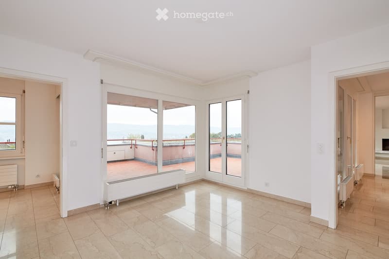 Empty room with white walls, tiled floor, large windows, and sliding glass doors leading to a balcony with a scenic view.