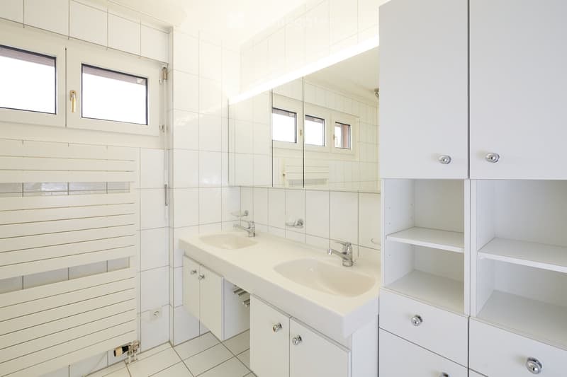 Modern bathroom with white tiles, double sink, mirrored cabinet, and built-in storage.
