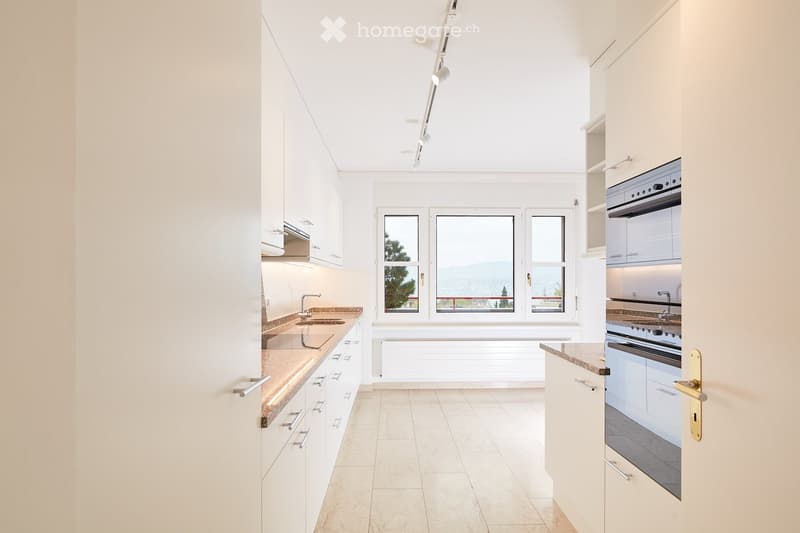 Modern, well-lit kitchen with white cabinets, a sink, an oven, and large windows offering a scenic view.