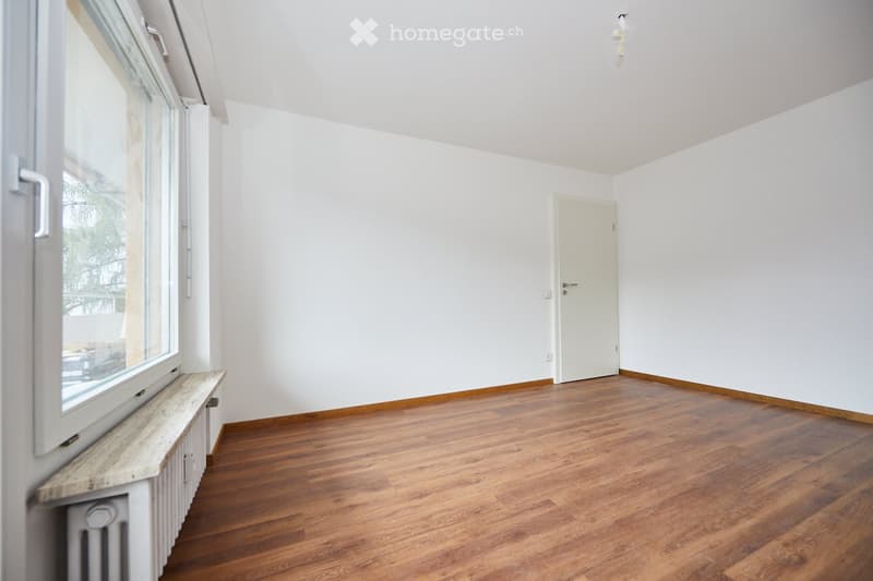 Empty room with white walls, hardwood floors, large window, closed door, heater.