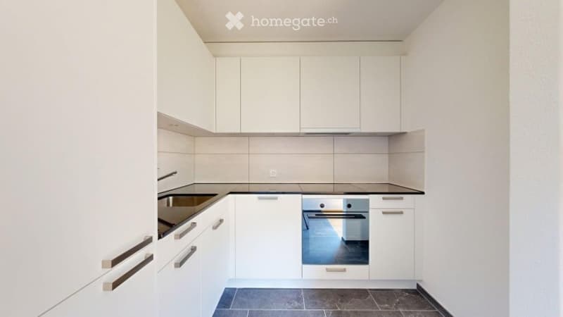 Modern kitchen with white cabinets, a stainless steel sink, and a built-in oven. The countertops are black, and the floor is tiled in dark blue.