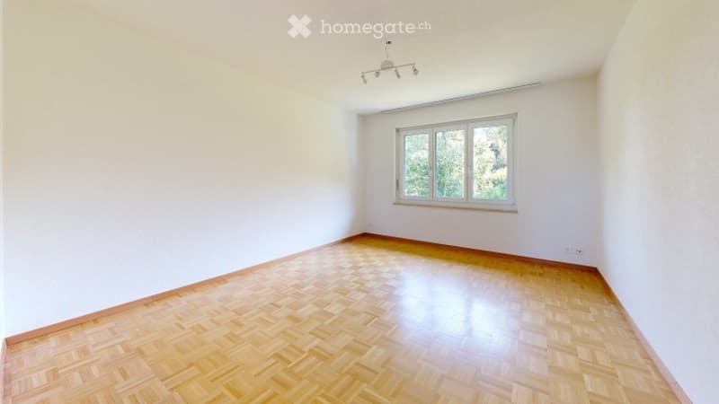 Empty room with wooden parquet flooring, white walls, and a single window with white frame. No furniture or equipment present.