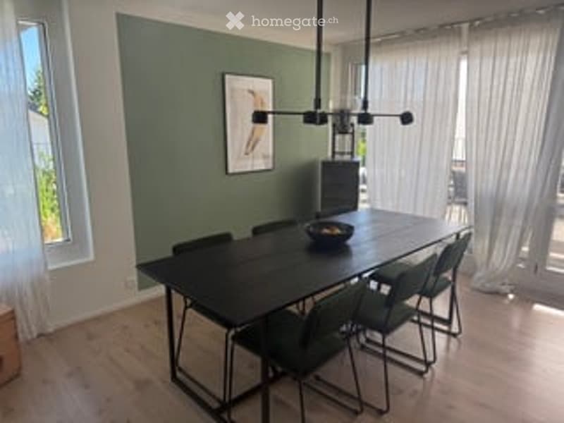 Dining room with dark green walls, wooden floor, large window with white curtains, modern black dining table with six chairs, a bowl on the table, and a picture frame on the wall.