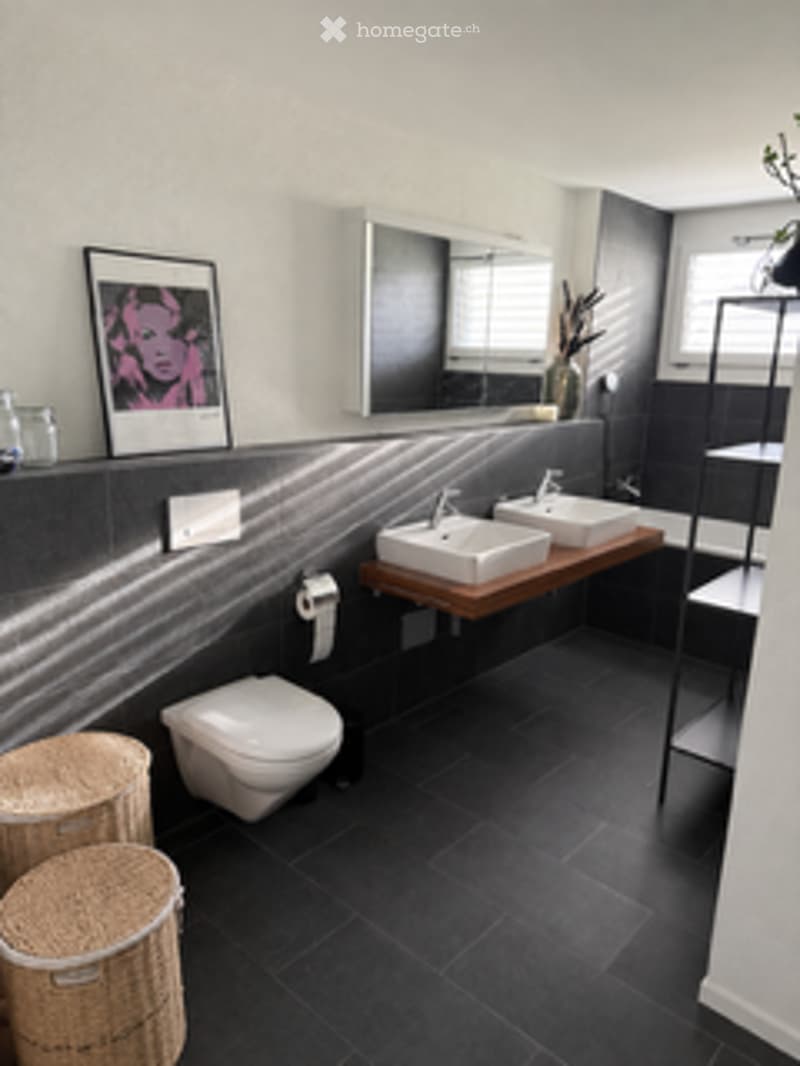 Modern bathroom with black tiled floor, double sink vanity, large mirror, toilet, and decorative wicker baskets.