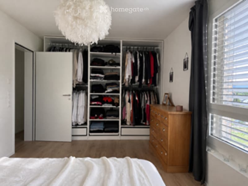 Bedroom with a large built-in wardrobe, a neatly made bed, a wooden dresser, and a hanging decorative lamp.