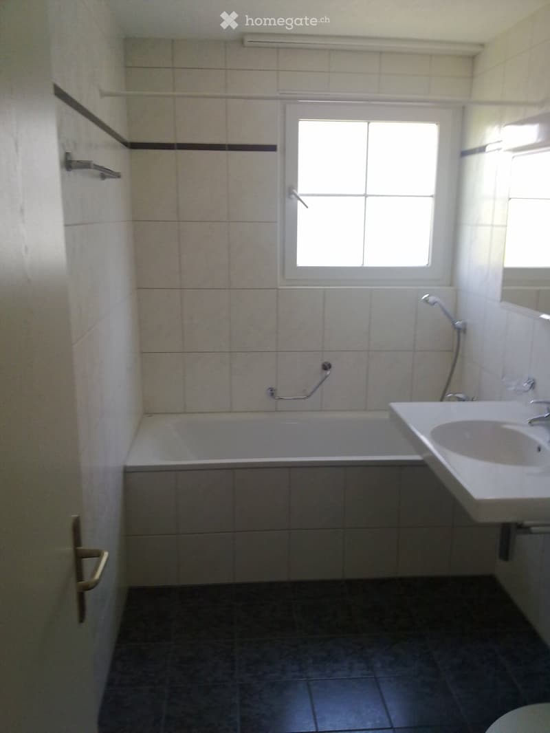 Bathroom with a bathtub, sink, and showerhead. The walls are tiled, and there is a window above the bathtub.