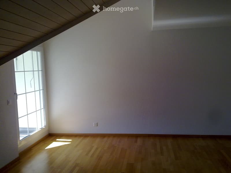 Empty room with wooden flooring, white walls, and a large window allowing natural light to enter.