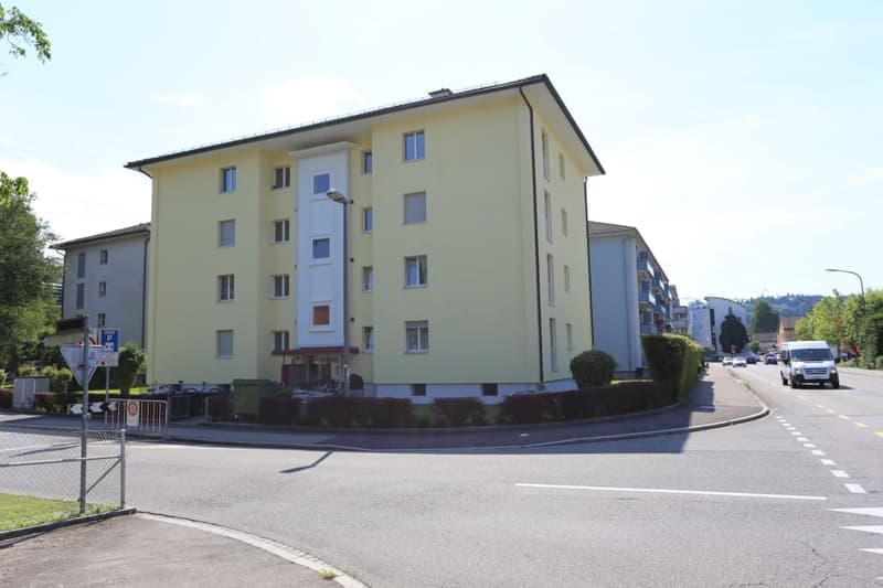 Four-story residential building with light yellow facade, multiple windows, and a small entrance area.