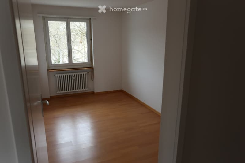 Empty room with wooden flooring, white walls, a window, and a radiator. No furniture or equipment present.