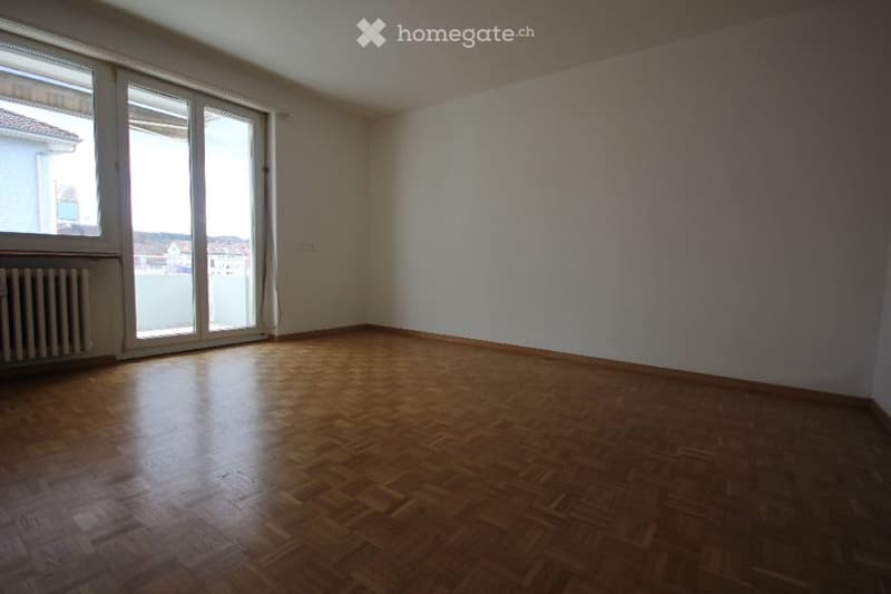Empty room with wooden flooring, large windows, and a radiator. No furniture or equipment present.