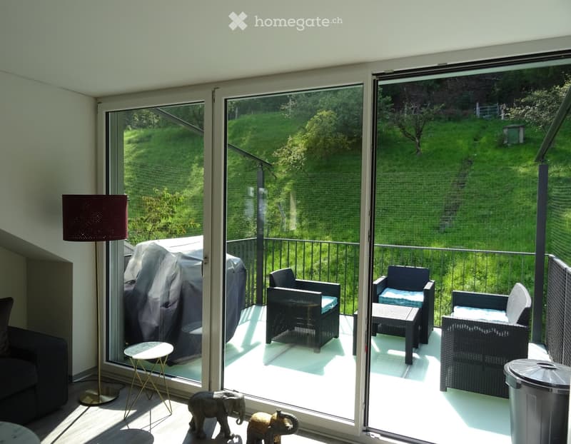 Balcony with wicker chairs, small table, and view of a green landscape.