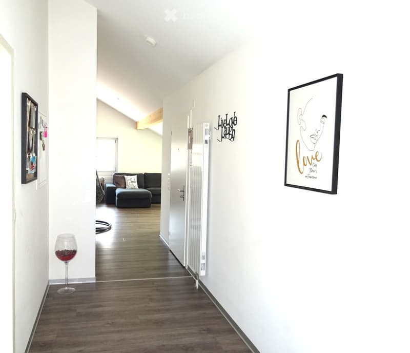 Bright hallway with wooden flooring, white walls, and modern decor including framed artwork and a wine glass on a side table.