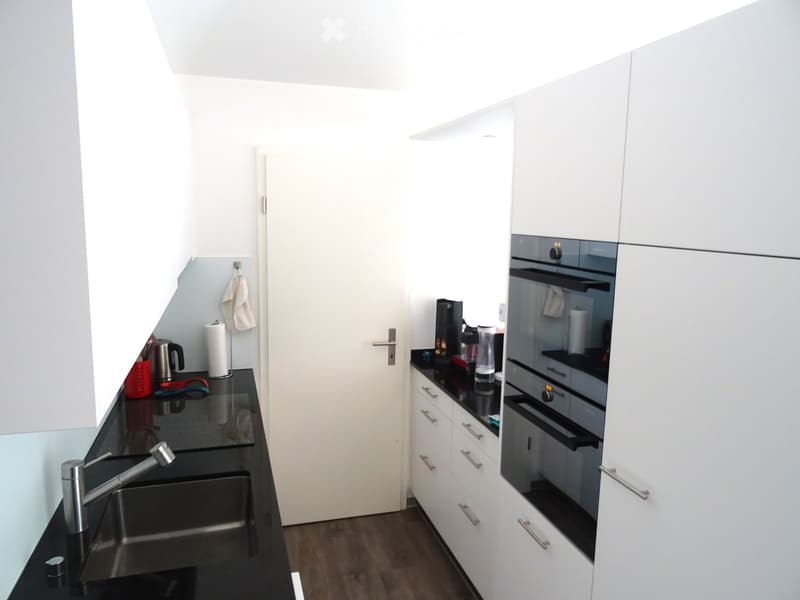 Modern kitchen with white cabinets, black countertops, stainless steel sink, and built-in oven.
