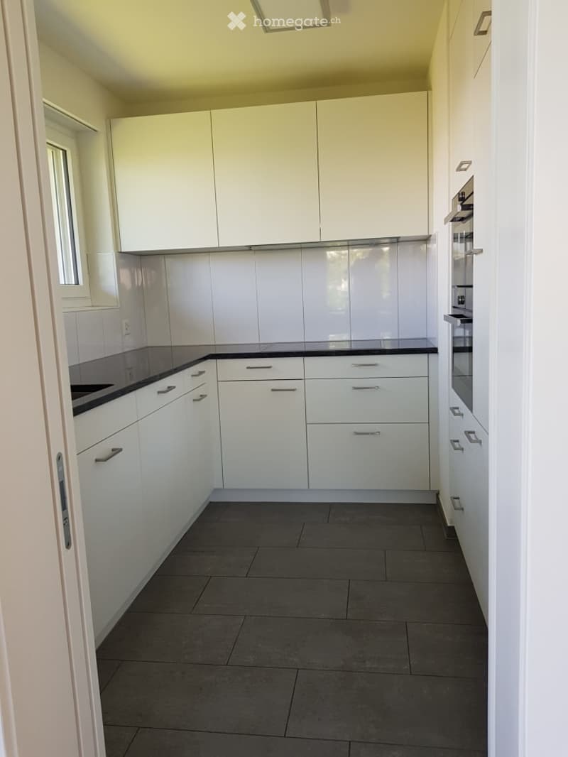 Modern kitchen with white cabinets, black countertops, and dark tiled flooring. Features include a built-in oven and a sleek, minimalist design.