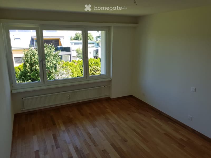 Empty room with wooden flooring, large windows, radiator, and neutral-colored walls.