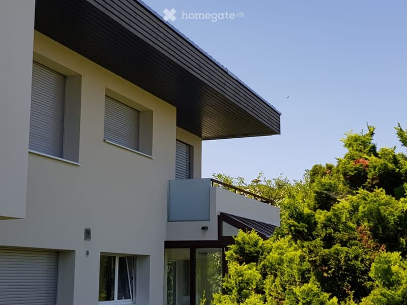 Modern two-story house with white exterior, grey roof, and balcony on the upper level.