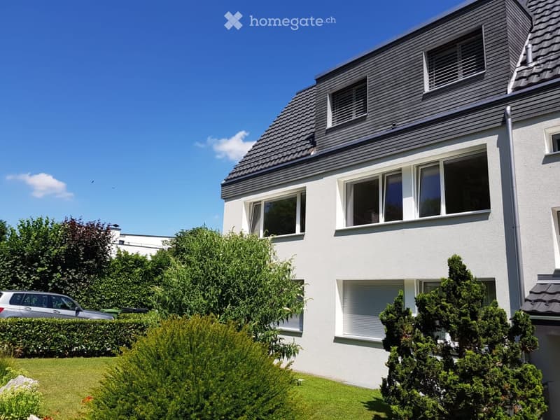 Modern two-story house with white exterior, grey roof, large windows, and a well-maintained garden with a parked car.