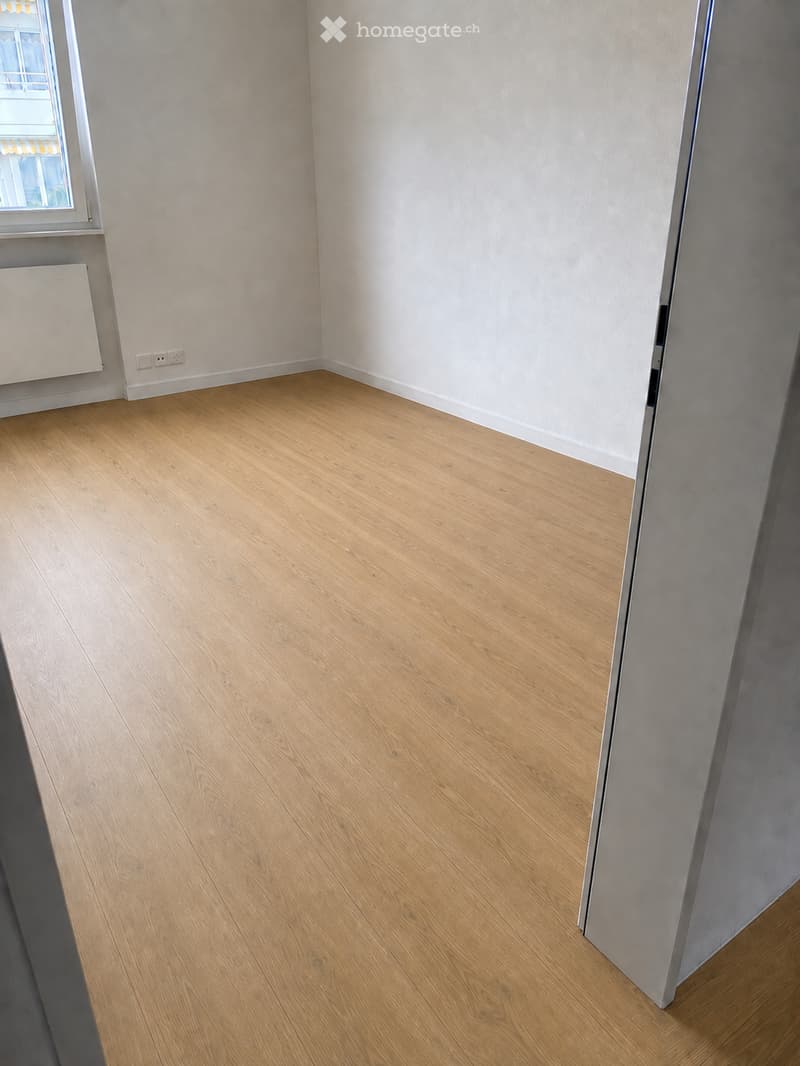 Empty room with light wooden flooring, white walls, and a window with a radiator below it.