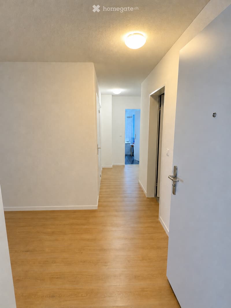 Clean, well-lit hallway with wooden flooring, white walls, and recessed lighting. Doors on both sides lead to other rooms.