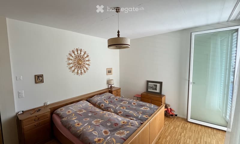 Bright bedroom with two single beds, wooden nightstands, a hanging lamp, wall decorations, and a small toy near the window.
