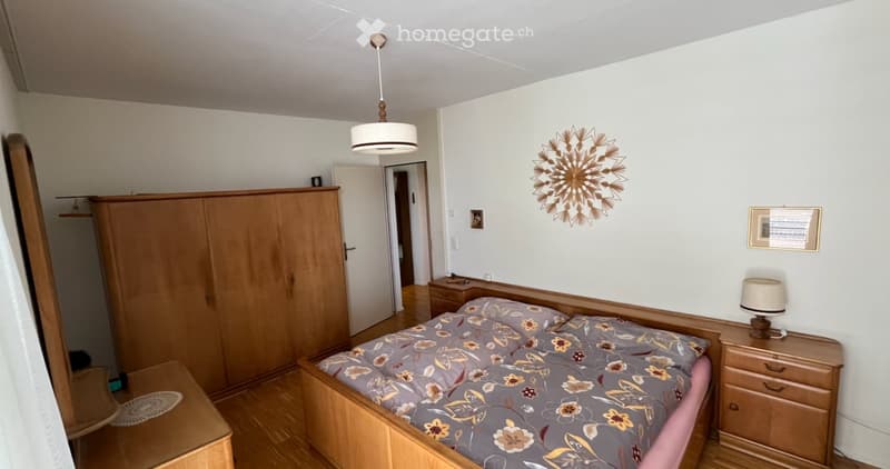 Cozy bedroom with wooden bed, floral bedding, wardrobe, nightstand, and wall decoration.