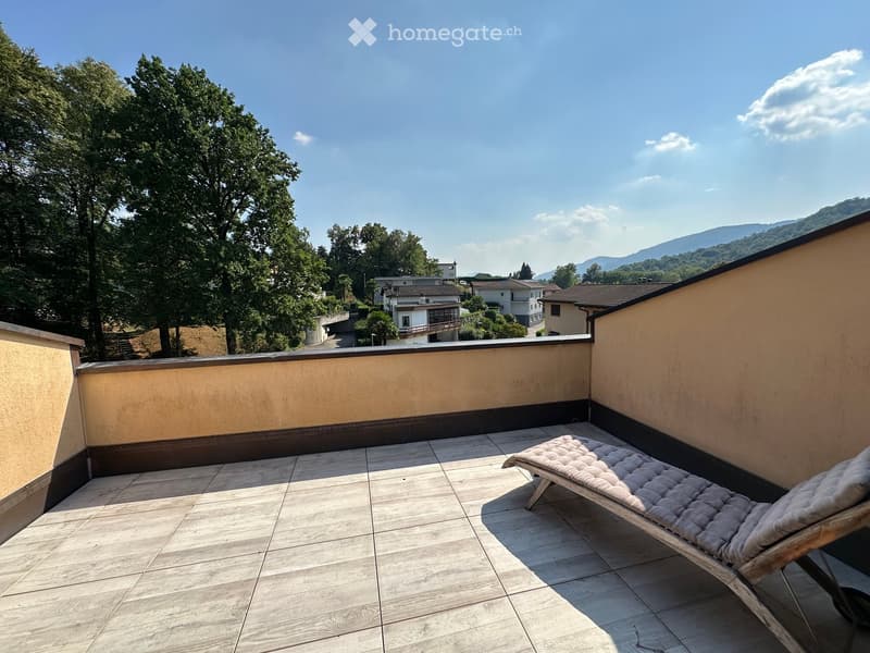 Balcony with tiled floor, sun lounger, and scenic view of trees and houses.