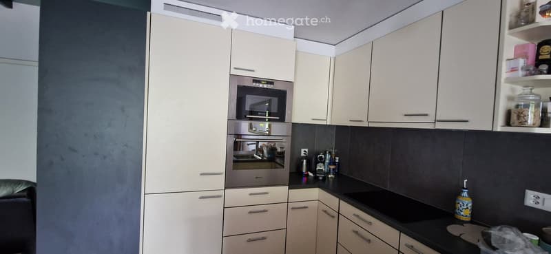 Modern kitchen with white cabinets, stainless steel oven, black countertop, and various small items on the counter.