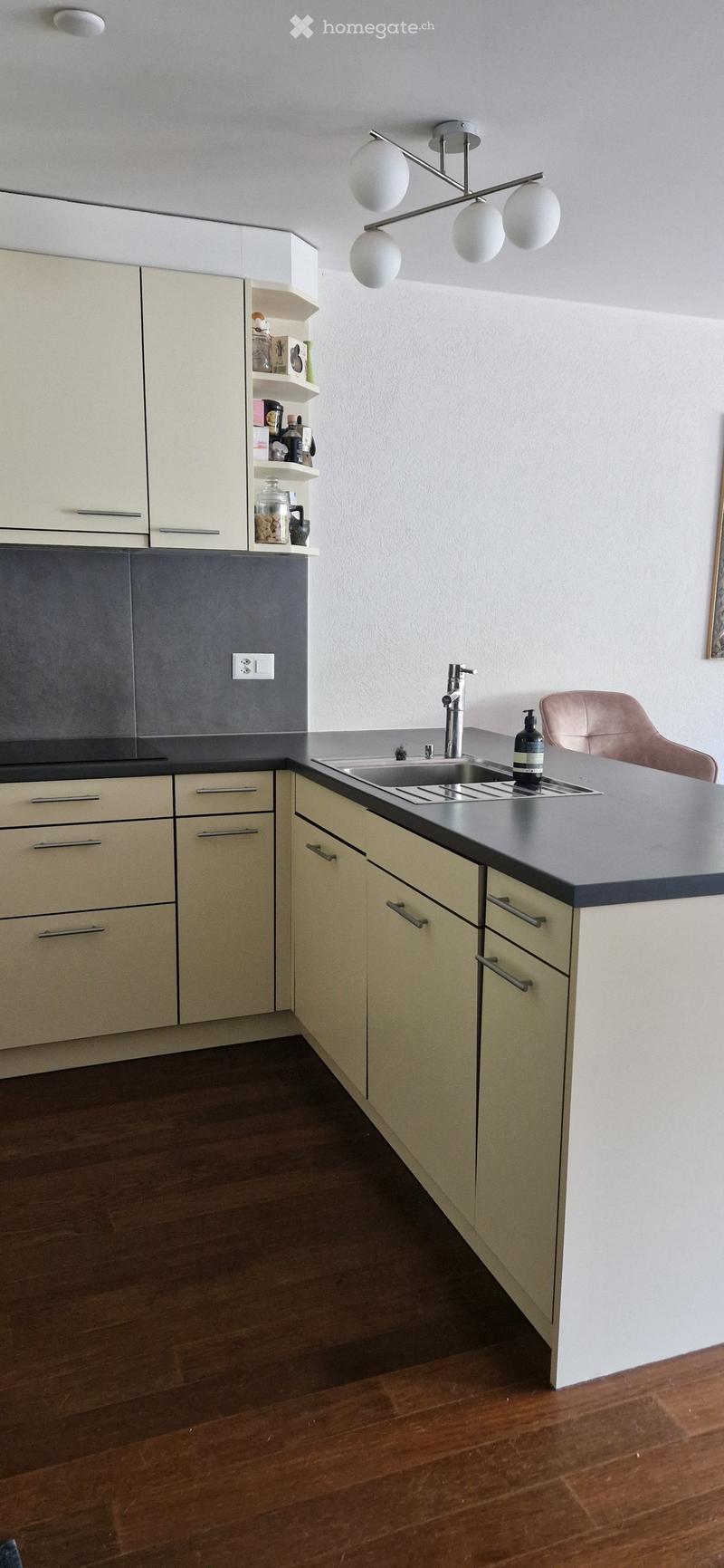 Modern kitchen with light-colored cabinets, a dark countertop, a sink with a modern faucet, and a decorative light fixture above.