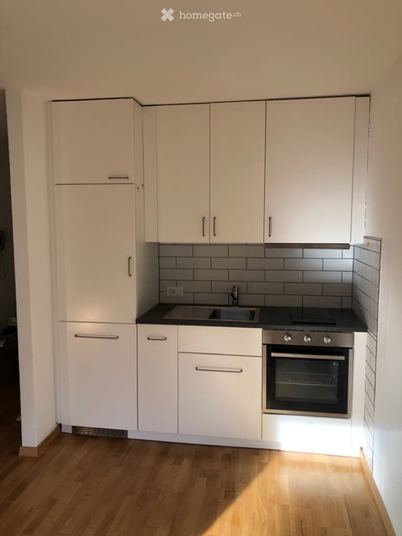 Modern kitchen with white cabinets, black countertops, a sink, a stove, and an oven. The floor is wooden.