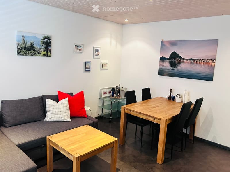A modern living room with a grey sofa, wooden coffee table, dining table with chairs, and several picture frames on the walls.