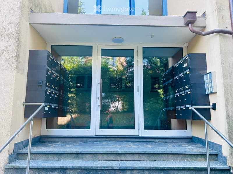 Entrance to a building with glass doors, mailboxes on either side, and a small staircase leading up to the entrance.