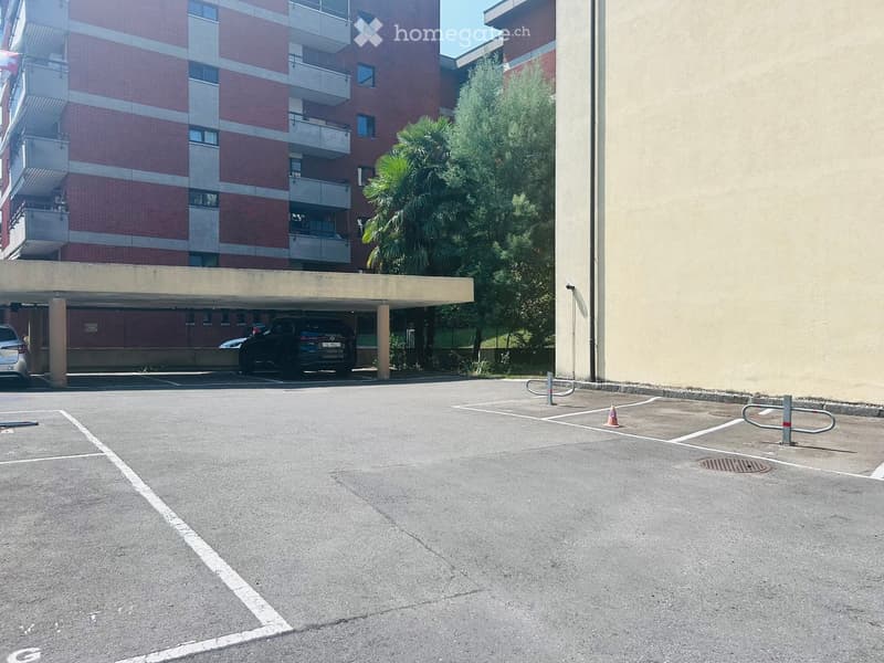 Parking area in front of a multi-story residential building with balconies and a covered garage area.