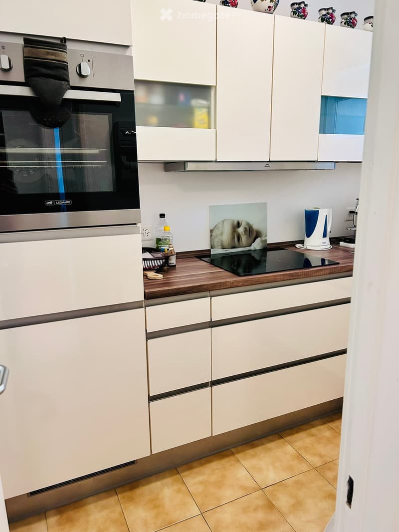 Modern kitchen with white cabinets, wooden countertop, induction stove, oven, and various small appliances and items on the counter.
