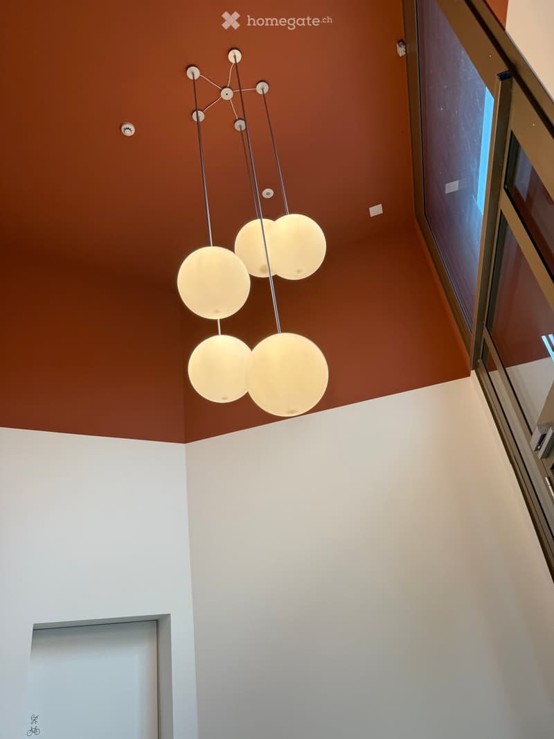 Empty room with white walls, a modern geometric light fixture, and a window with blinds.