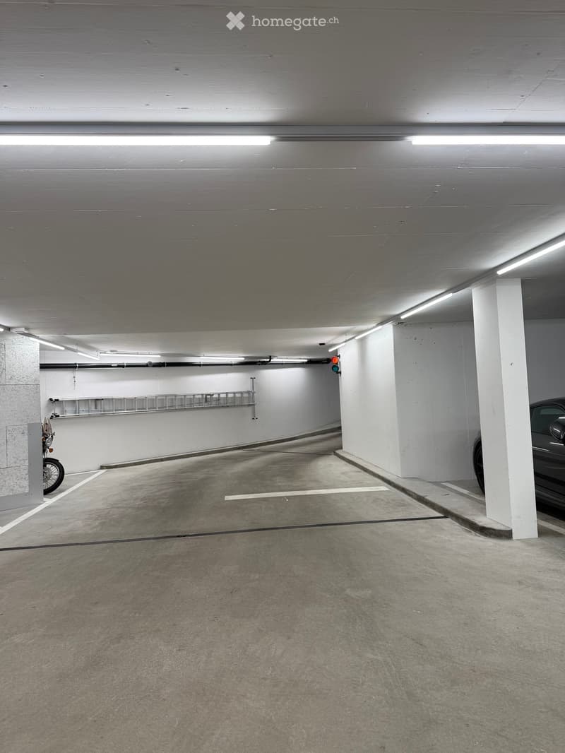 Underground parking area with concrete floors and walls, marked parking spaces, and a few vehicles including a motorcycle and a car.