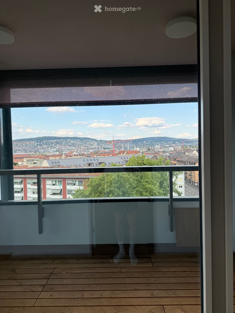 Balcony with wooden decking, glass railing, and panoramic city view.