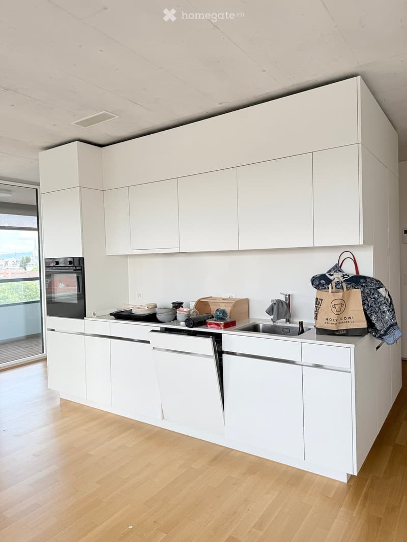 Modern kitchen with white cabinets, stainless steel appliances, wooden countertops, and a large window overlooking a cityscape.