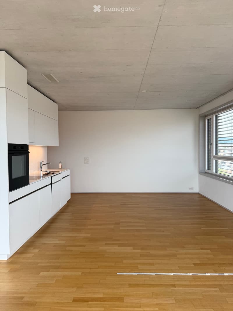 Empty kitchen with white cabinets, wooden floor, and a window with blinds. No furniture or appliances are present.