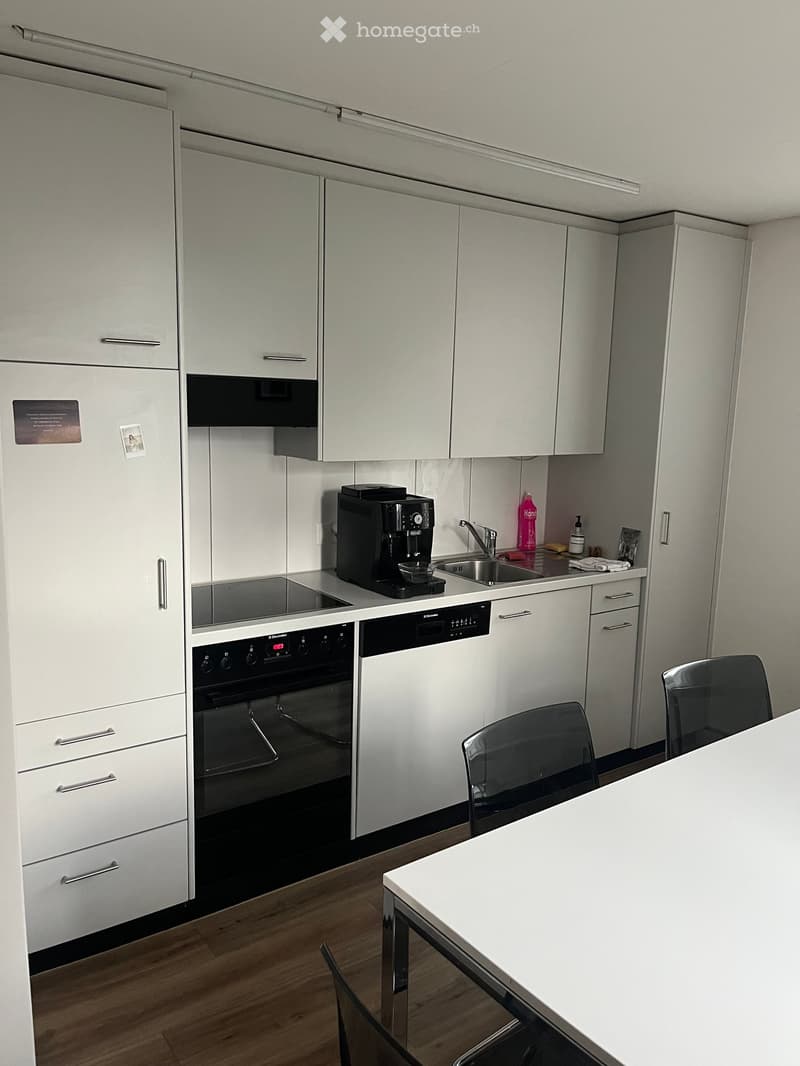 Modern kitchen with white cabinets, stainless steel appliances, a coffee machine, and a small dining area with a table and chairs.