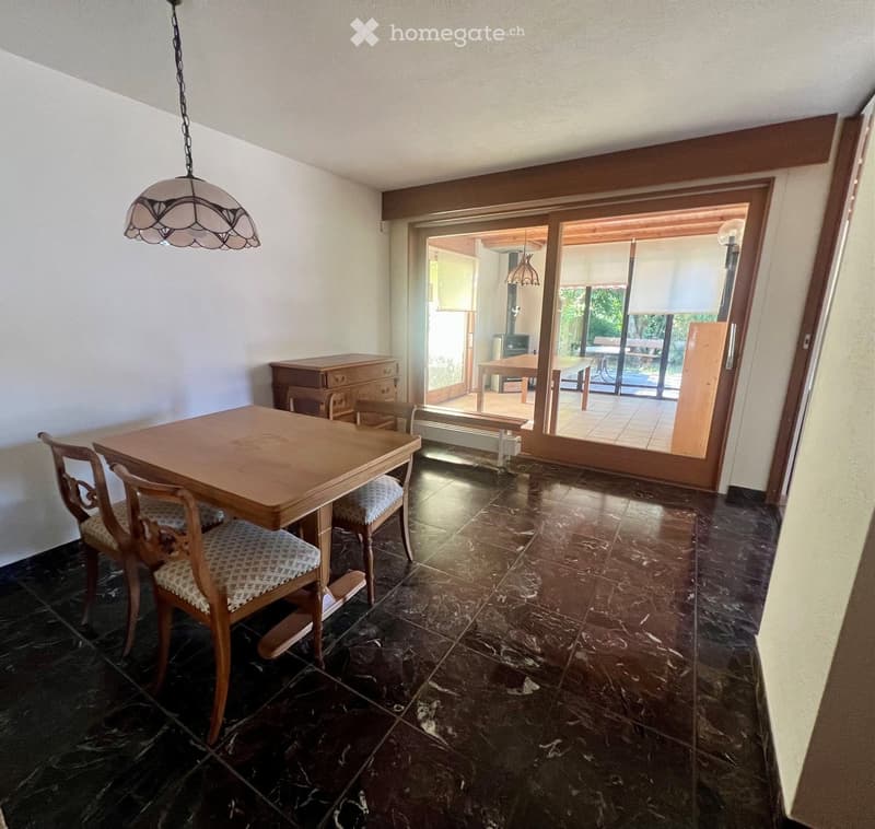 Dining room with a wooden table, chairs, a cabinet, and a hanging lamp. Large sliding glass doors lead to a patio area with outdoor furniture.