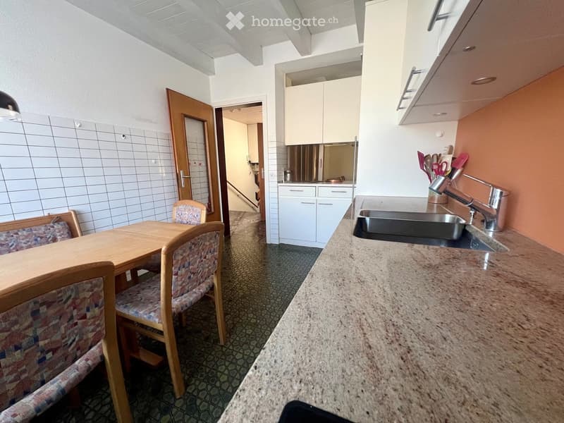 A small kitchen and dining area with a wooden table, four chairs, a sink, and cabinets.