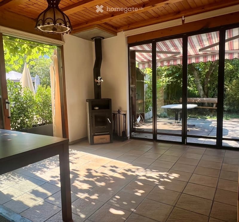 Bright living space with tiled floor, large sliding glass doors leading to outdoor area, fireplace, and a table.