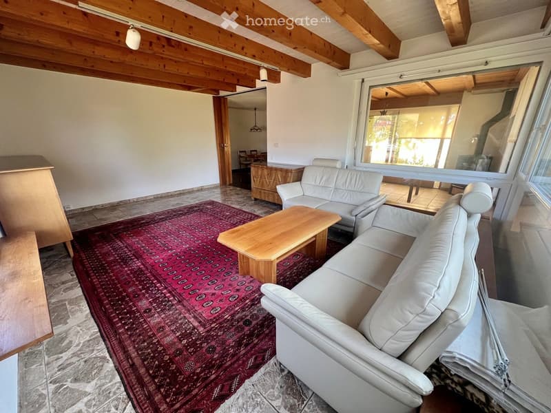 Living room with a white leather sofa, wooden coffee table, red patterned rug, and a wooden cabinet in the background.
